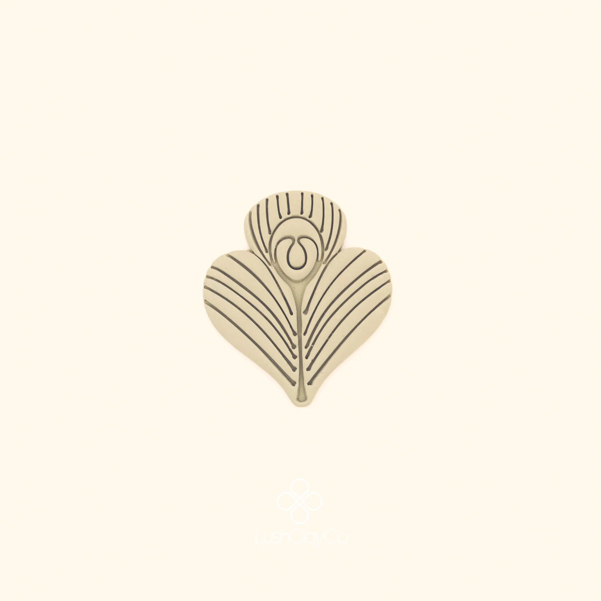 Clay impression of the Tavus Tüyü peacock feather cutter showing dense parallel radiating lines and central oval eye pressed into polymer clay