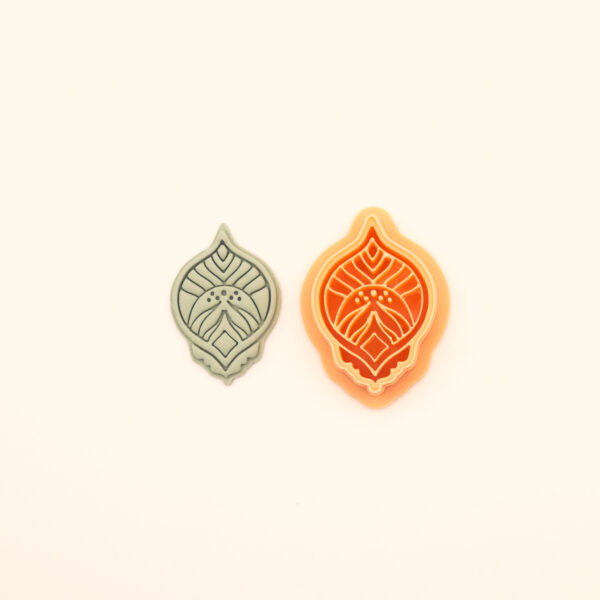 Zerrin hatayi polymer clay cutter alongside clay impression showing pointed oval silhouette with central diamond form, curved leaf detail and dot clusters